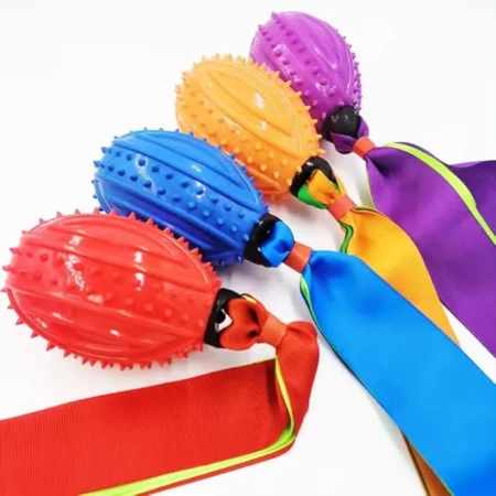 Four football-shaped rubber dog toys with spikes and attached fabric ribbon tails in red, blue, orange, and purple, arranged on a white background.